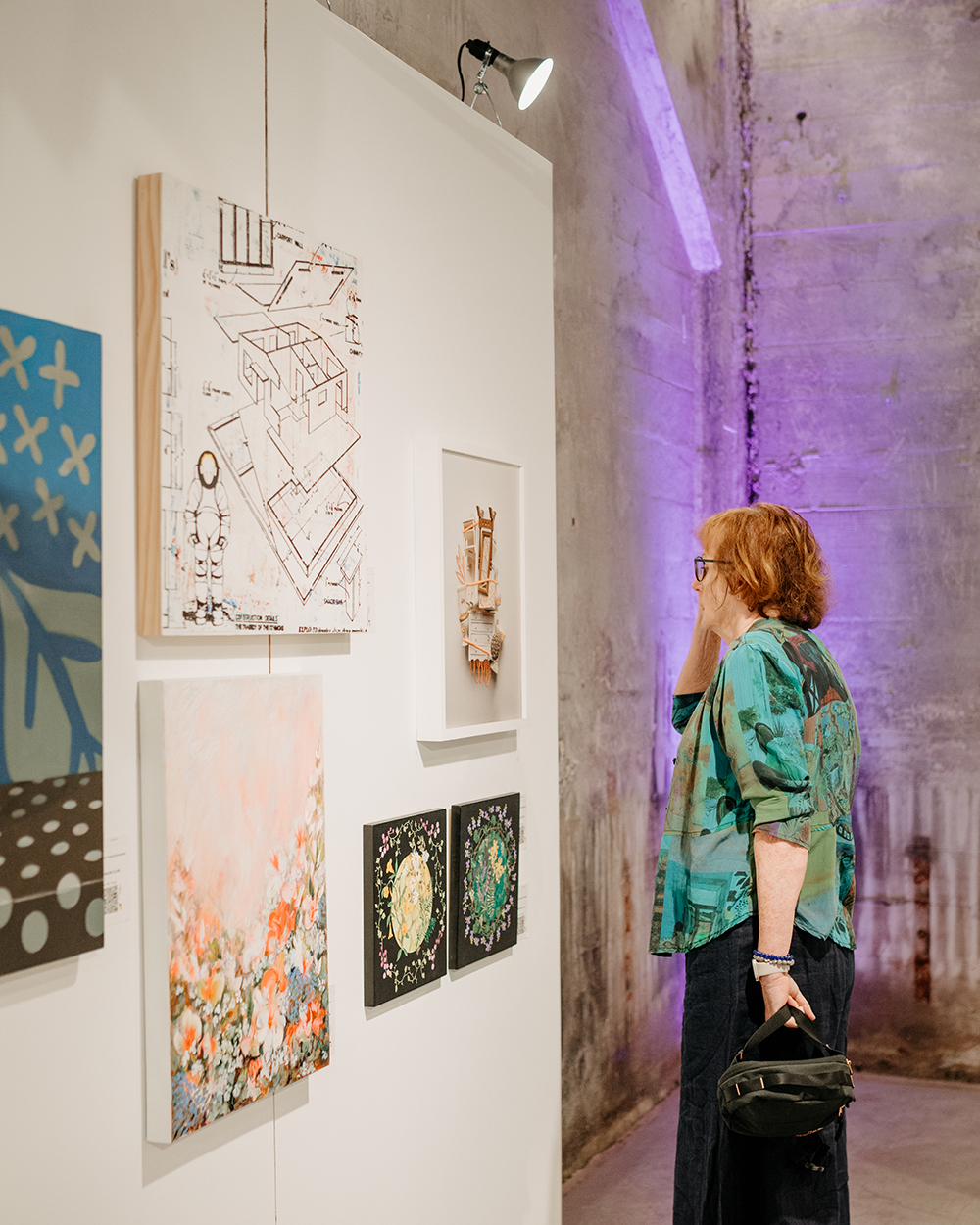 A woman looks at painting on a gallery wall.