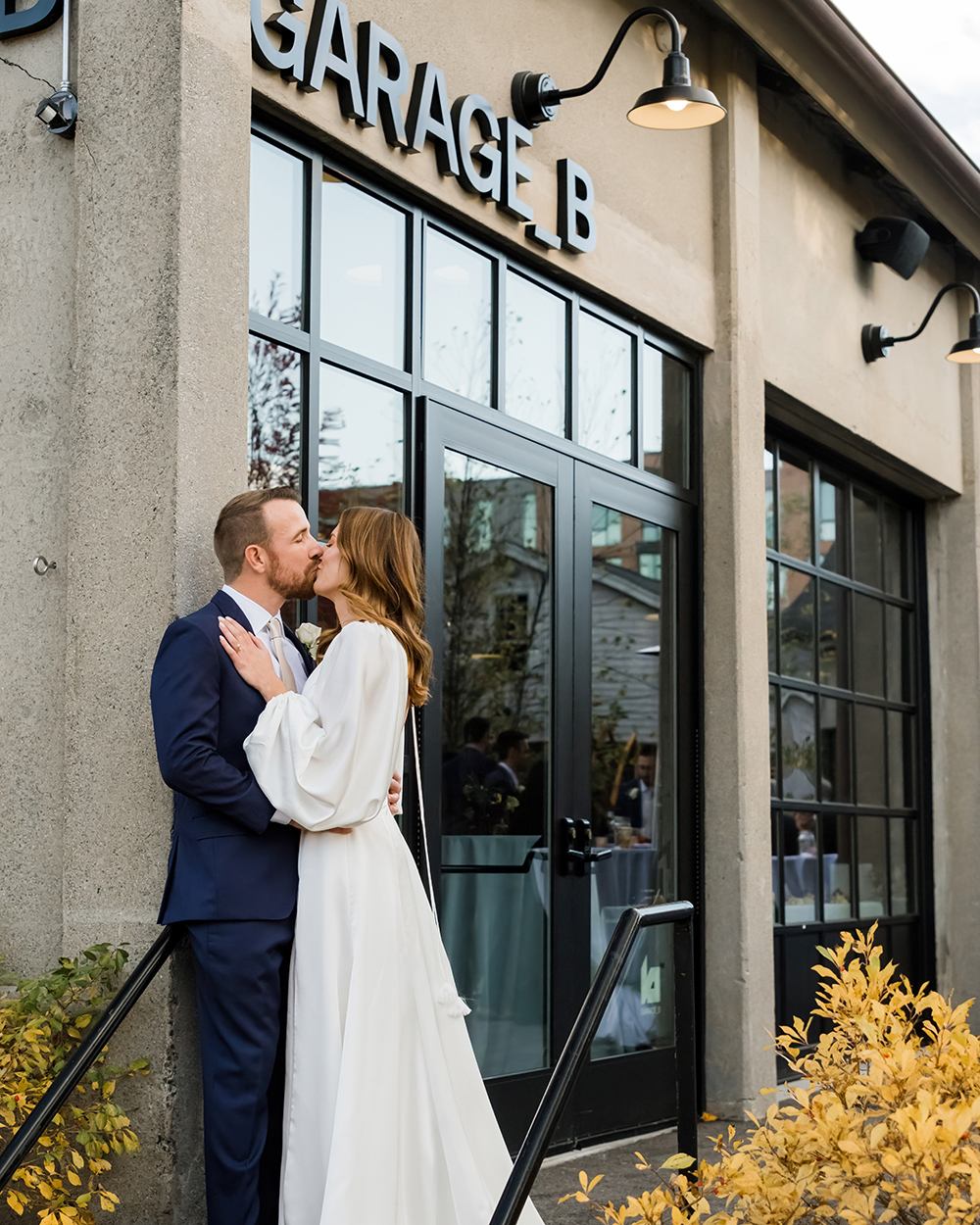 A groom and bride kiss at the exterior of Garage B with the venue's signage above them.
