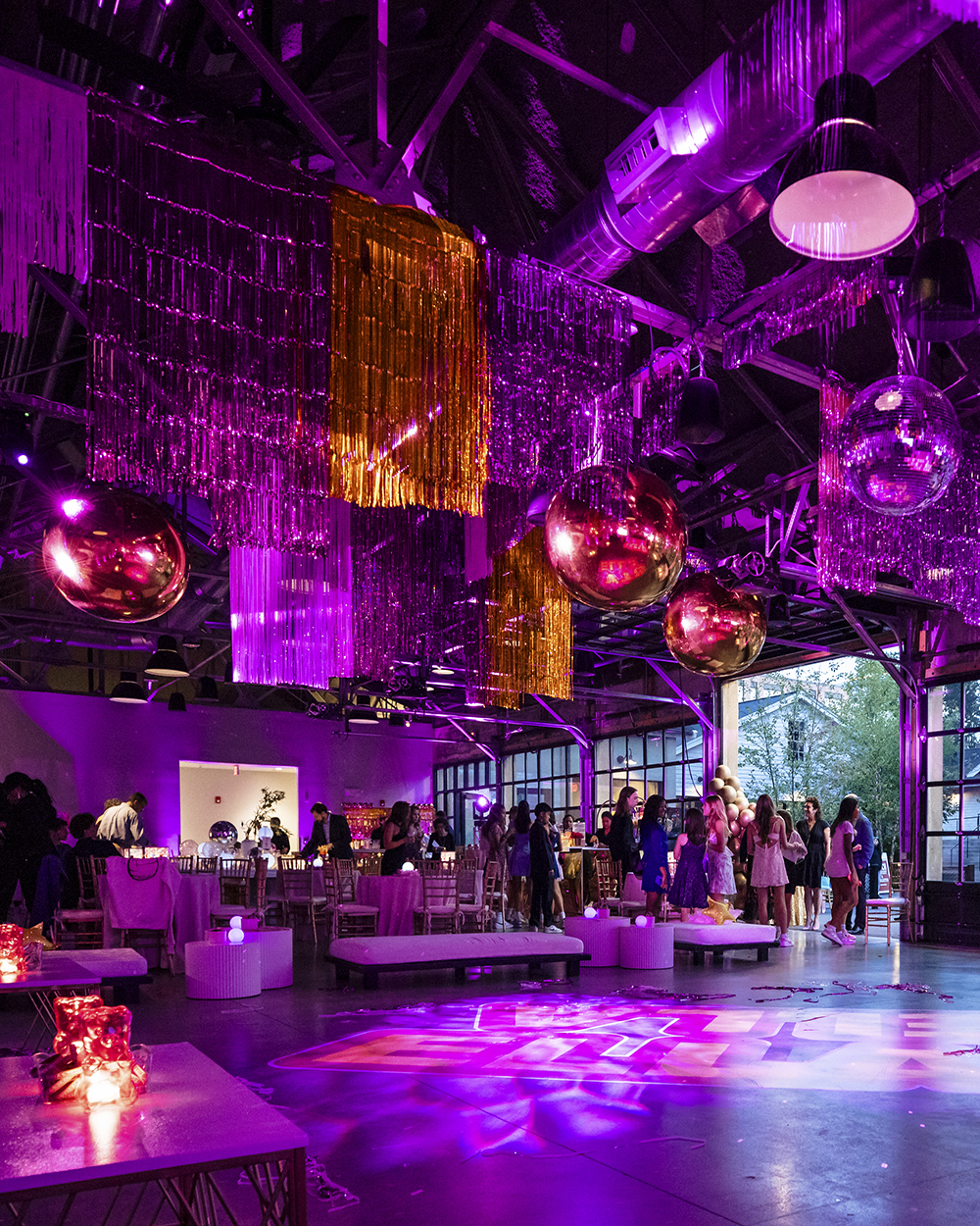 An ongoing bat mitzvah in a venue filled with purple and pink lighting and matching disco ball and streamer decor.