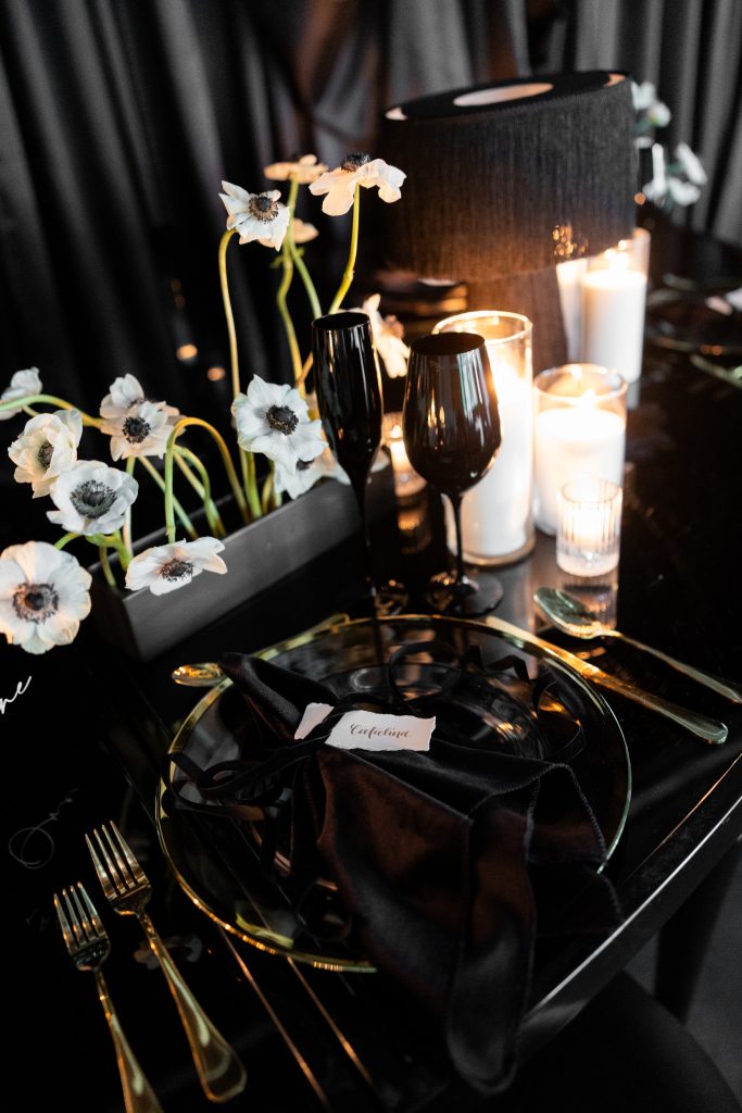 A monochromatic tablescape in black and white with anemones, fringe table lamps, pillar candles, and dinnerware with gilded details.