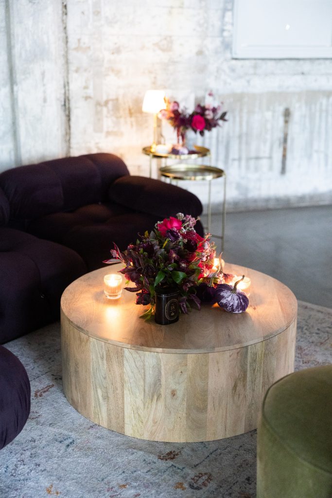 A lounge area with a wooden, circular coffee table topped with a floral centerpiece.