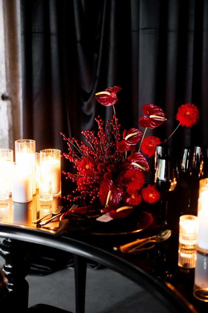 A tablescape with a red asymmetric floral centerpiece flanked by arrangements of candles.