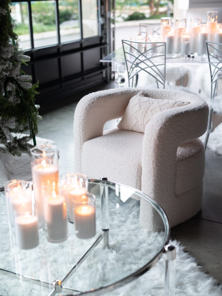 A fuzzy accent chair with matching argyle-patterned throw pillow seated by an acrylic coffee table topped with pillar candles.