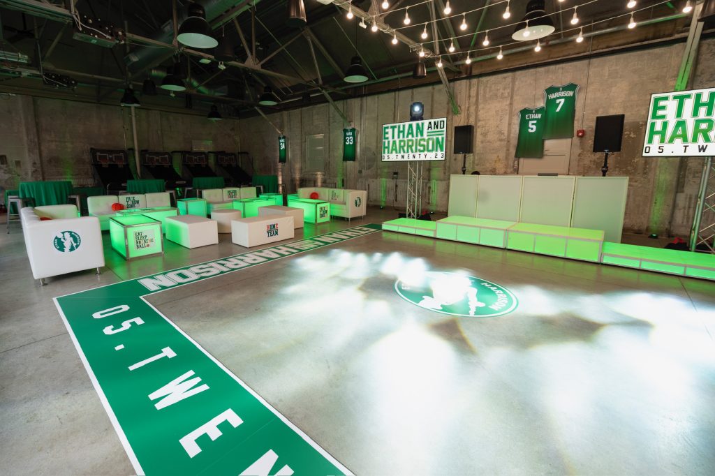 A bar mitzvah setup, including DJ booth and lounge area, in a warehouse-style venue decorated with a Boston Celtics theme.