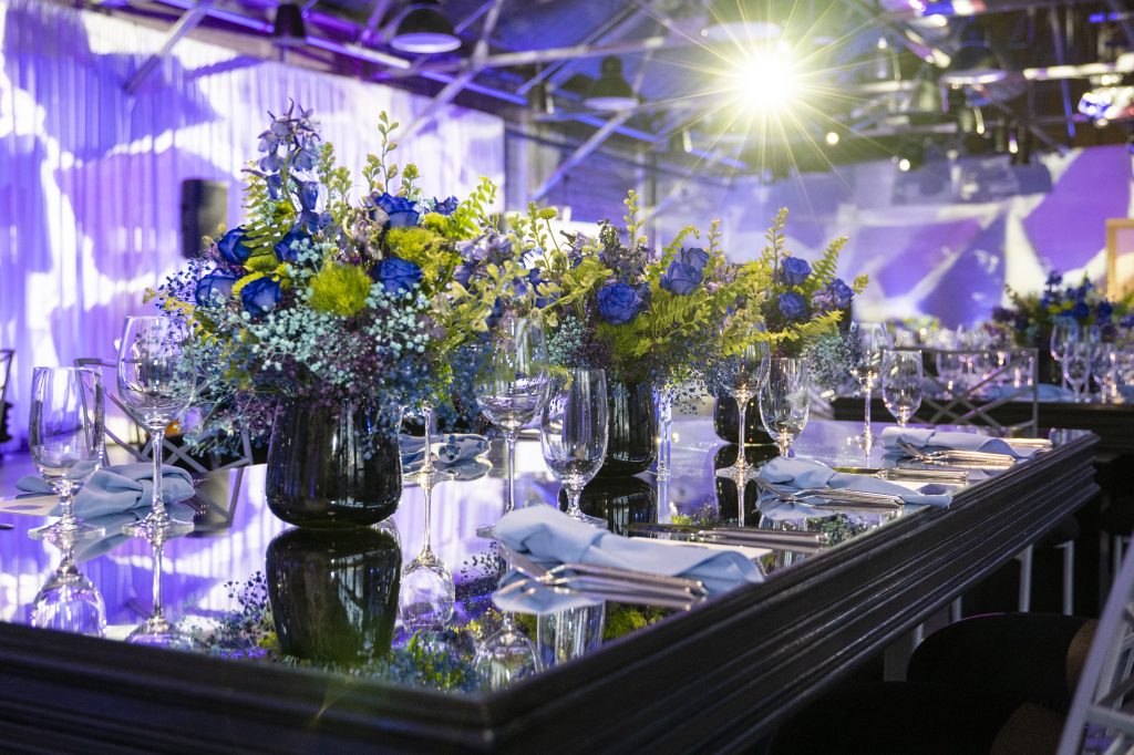 An arrangement of floral centerpieces along a banquet table with a mirror top.