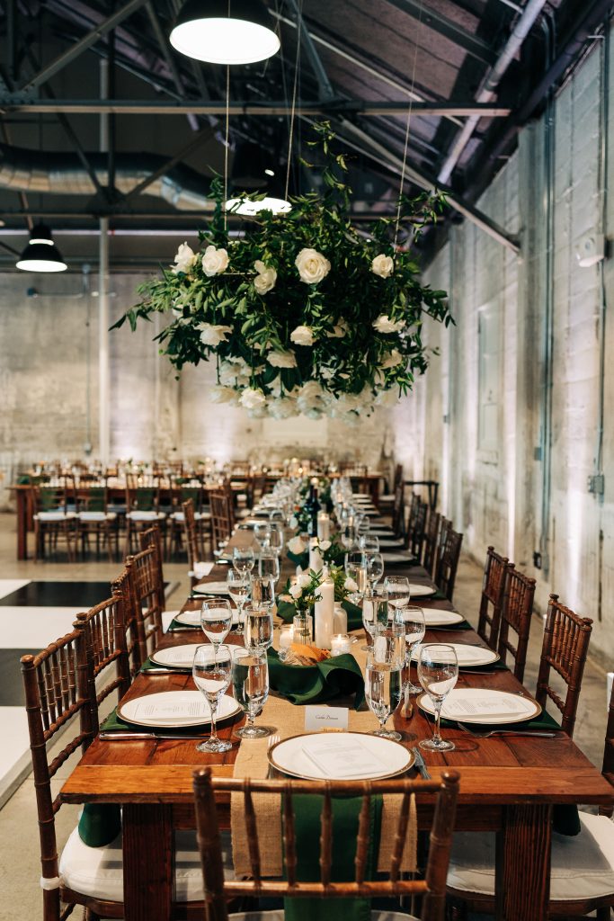 A floral arrangement hangs over a long wooden banquet table at a wedding reception.