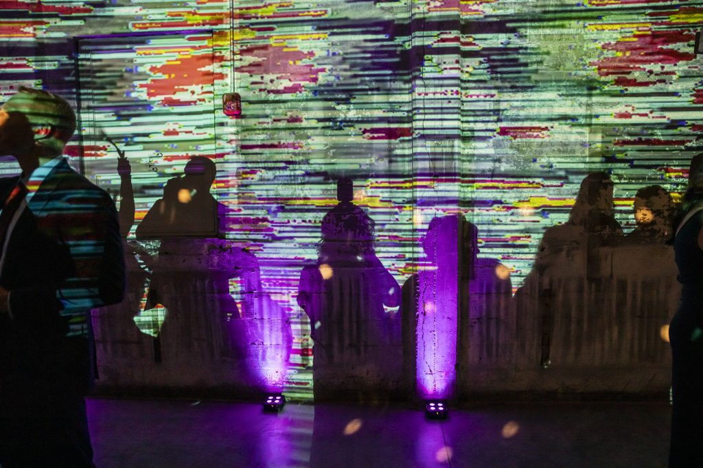 Several people's shadows cast upon a colorful abstract design projected onto a wall.