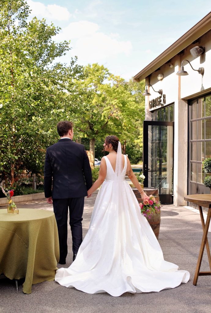 A groom and bride walk hand-in-hand on a patio adjacent to Garage B's exterior.