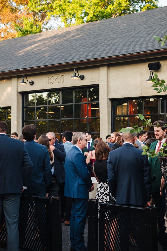 Wedding guests mingle on a patio adjacent to a warehouse-style venue.