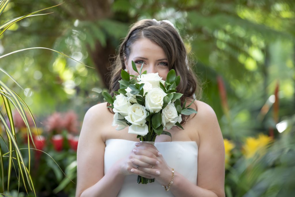A bride with smiling eyes holds her bouquet up to her face.
