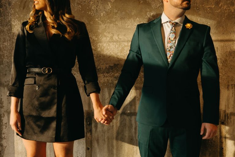The torsos of a woman and man standing hand-in-hand against a distressed stone wall