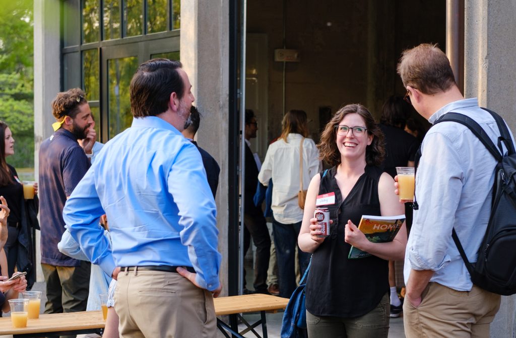 A group of people in business-casual attire mingle outside a venue while drinking alcoholic beverages.