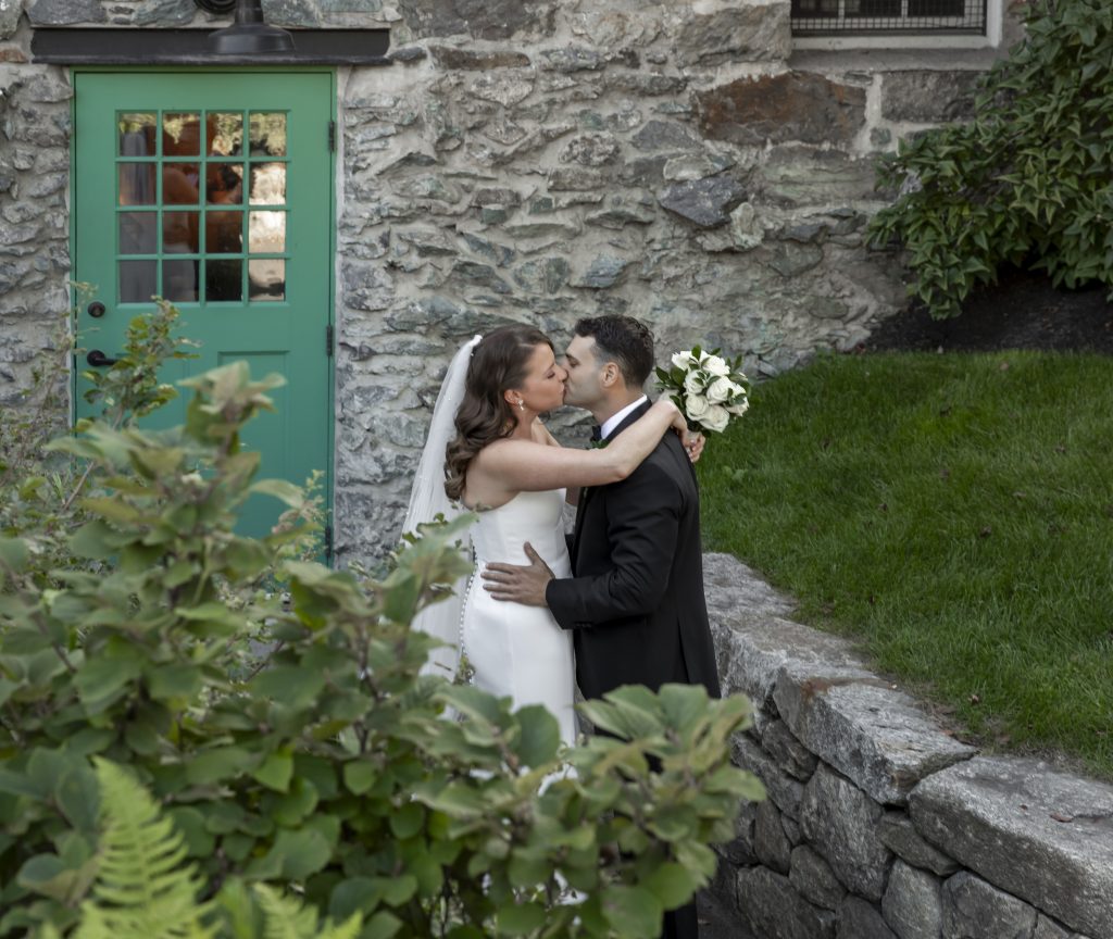 A bride and groom kiss at the exterior of a stone building.