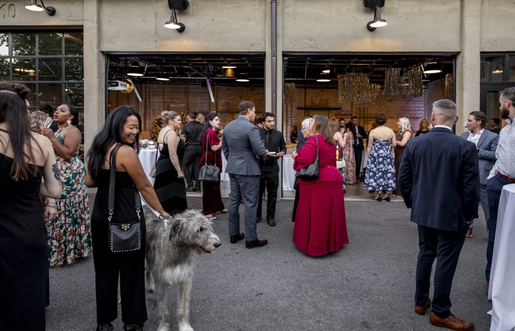 Wedding guests mingle on a patio outside a venue featuring a bank of open garage-style doors.