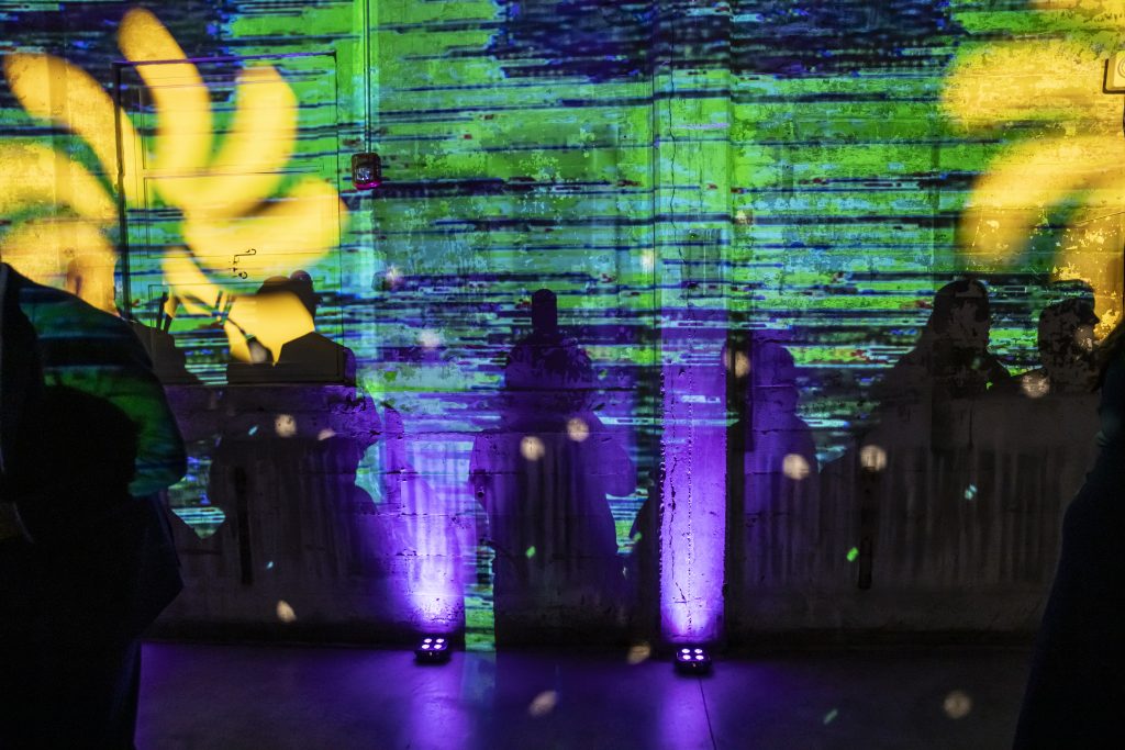 A colorful, abstract design is projected onto a stone wall, capturing the shadows of nearby people.