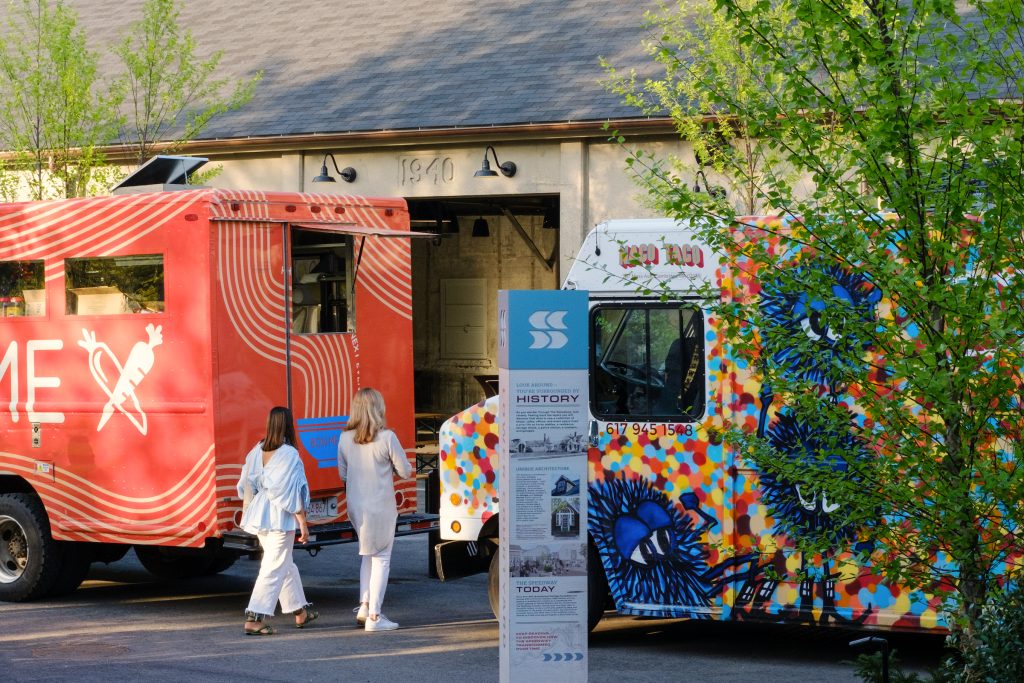 Two people enter a warehouse-style venue between two parked food trucks.