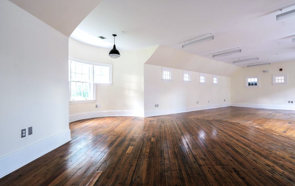 The interior of the Annex that features painted white walls, natural hardwood floors, cottage-style windows, and a rounded turret corner.