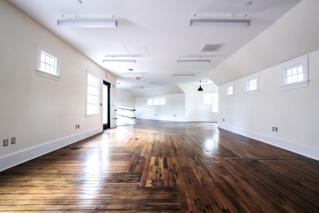 An empty, light-filled 1,000 SF room featuring white walls, cottage-style windows, natural hardwood floors, and a rounded turret corner.