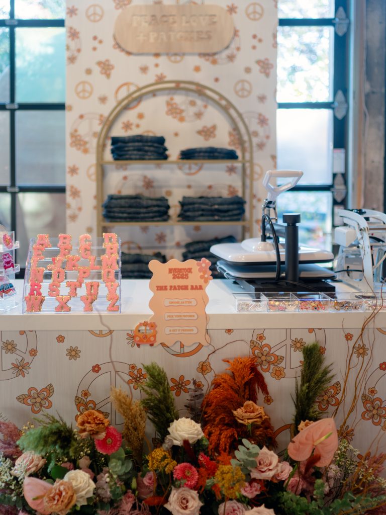 A custom-built heat press station, boasting denim jackets and monogram patches for customization, fronted by an arrangement of flowers.