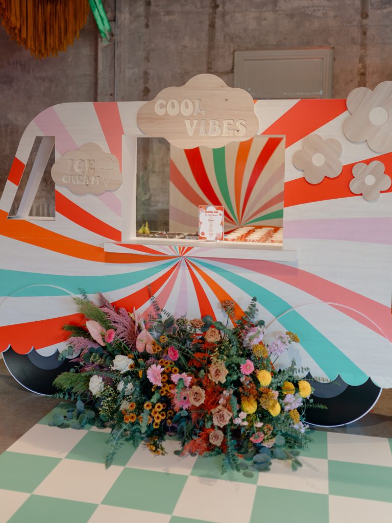 A custom-built ice cream stand styled after a truck fronted by a large arrangement of colorful flowers.