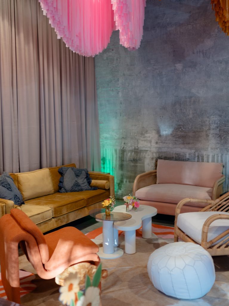 A lounge area against a draped, distressed stone wall that features a sofa and chairs with rattan accents, a curvilinear coffee table, and area rugs.