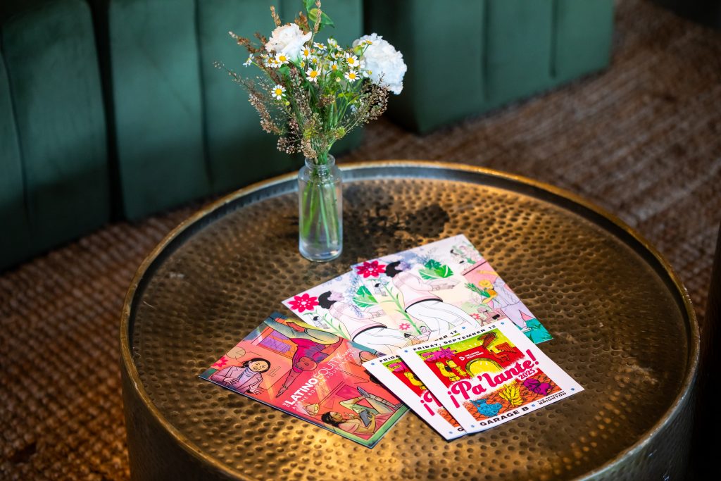 A round, rustic coffee table topped with a bud vase and event programs provided by the Latino Equity Fund.