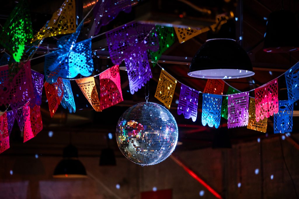 A disco ball and banners of papel picado hang from a ceiling among pendant lights.