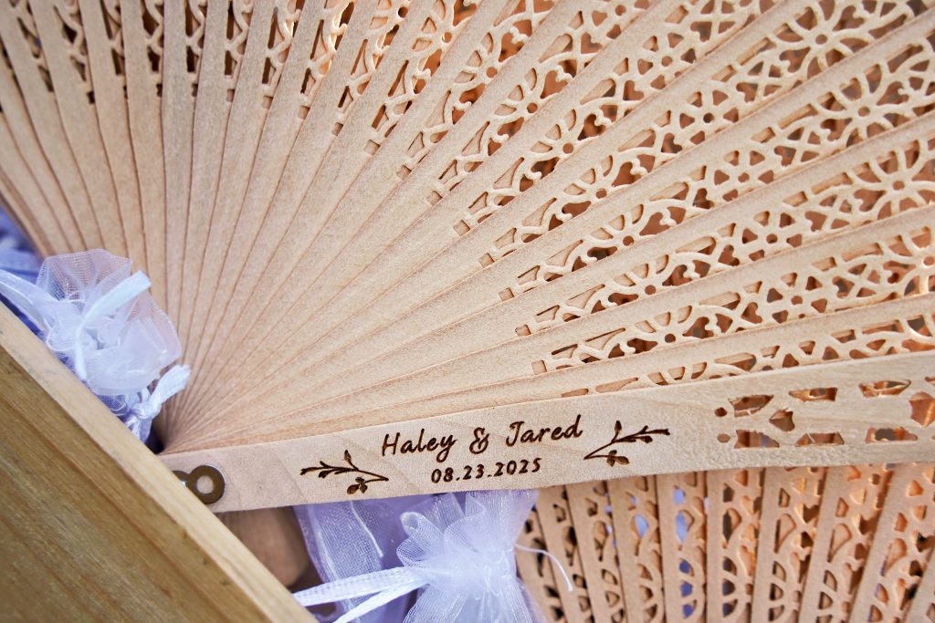 A wooden fan customized with the names "Haley & Jared" and the date of August 23, 2025.