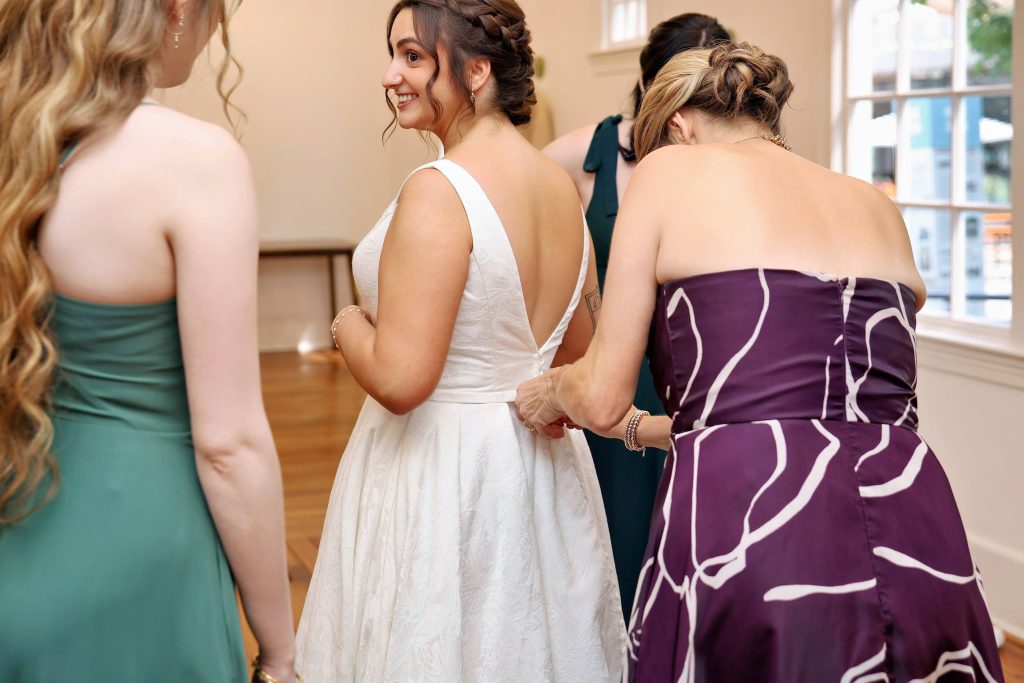 A bridal party tends to a woman's white gown as she smiles.