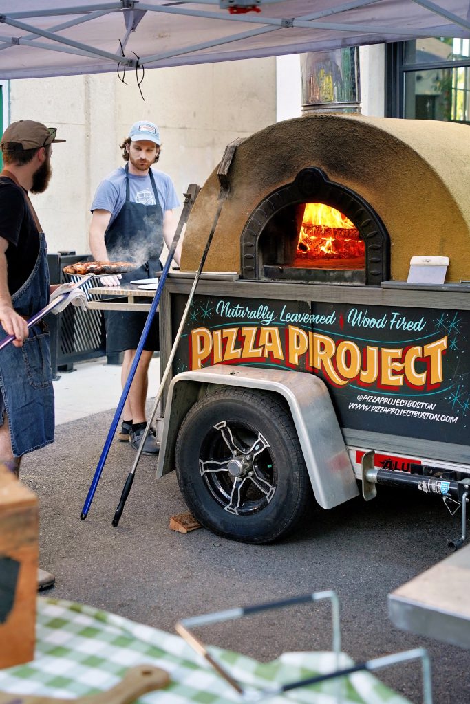 Two people work at Pizza Project's branded wood-fired oven.