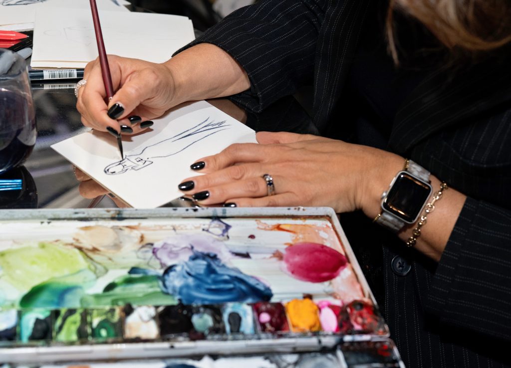 A close-up of a hand painting a watercolor silhouette of a person in a dress.
